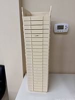 Stack of 24 cream plastic storage bins stacked vertically against a wall near a thermostat.