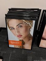 Front view of several black poster frames stacked together, one showing a poster with a woman's face.