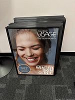 Stack of twelve black plastic poster frames with a promotional insert for Caryl Baker Visage Winter Skin Clinic inside one frame.