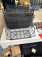 Top view of stacked black metal wire baskets on a white table, showing 10 units in total with handles on the sides.