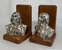 Front view showing two vintage bookends, each with a shiny metal bust of a Native American man mounted on wooden bases and back plates.