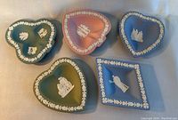 Five vintage Wedgwood Jasperware trinket dishes in various colors and shapes arranged on a surface, showing the white classical relief figures and floral borders.