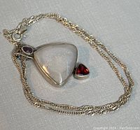 Full view of the necklace with the chain neatly coiled and pendant centered revealing its stones and silver chain clasp.