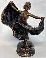 Front view of the bronze spelter dancer figurine showing outstretched arms and flowing skirt with gilt wear.