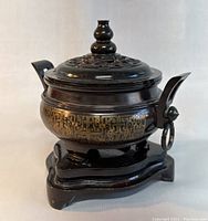 Front angled view of bronze censer on wooden stand showing decorative gold band and side handle with ring.