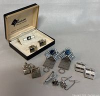 Full view of men's jewelry set including cufflinks, tie clips, and earrings arranged on white surface showing condition and details