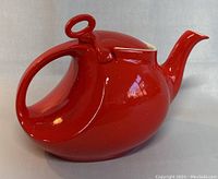 Side view of red ceramic teapot showing elegant curved handle, loop lid handle, and spout.