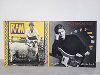 Front covers of two Paul McCartney vinyl records, 'RAM' showing Paul with a sheep and 'All The Best' showing Paul with bass guitar and stickers.