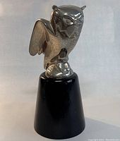 Front view of signed metal owl sculpture perched on black wooden stand.