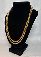 Overall view of long gold plated rope chain necklace on black stand.