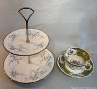 Photo showing two-tier cake stand with silver handle and blue floral design alongside EB Foley teacup and saucer