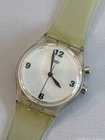 Close-up view of the watch dial and strap showing clear plastic case, white dial, and light green translucent strap.