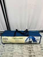Blue and white hexagonal dome tent in a protective blue carry bag with label showing product details and picture of assembled tent.