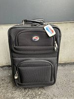 Front view of black American Tourister carry-on luggage showing two zippered compartments and logo tag.
