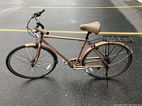 Full side view showing the metallic bronze frame, brown saddle, grips, and fenders, 700c tires, rear rack, and overall bike geometry on black asphalt surface.