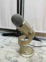Front right-angle view of gold Blue Yeti microphone on integrated stand showing metal mesh grille and adjustment knobs.