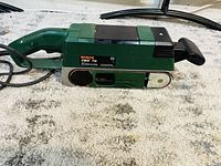 Side view of green Bosch PBS 75 belt sander showing general shape, handle, and power cord.