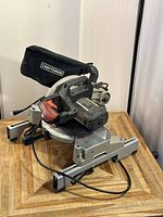 Front angled view of Craftsman miter saw on workbench with dust bag and power cord visible.