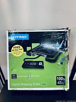 Front view of retail box showing Dymo S100 digital shipping scale packaging with some damage and creases.