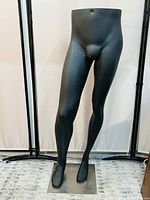 Front view of black male mannequin lower body with visible light scratches, mounted on metal stand.