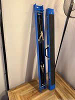 Two blue metal sawhorses folded flat, standing upright showing the side with handles and metallic folding braces.