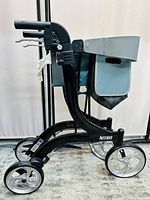 Side view of Drive Nitro rollator walker showing black frame, silver wheels, grey padded seat, side pouch, and hand brakes.