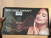 Box of red light therapy device showing features such as auto timer, adjustable brightness, angle, and height, with a smiling woman image on the packaging.