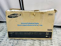 Front of worn and taped Samsung Professional Display 32-inch cardboard box with branding and model details visible.