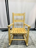 Front view of wooden toddler rocking chair showing slatted seat, backrest, and armrests in light natural wood.