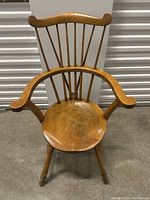 Front view of the antique wooden armchair showing the curved backrest with vertical spindles, the round seat, and turned legs.
