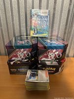 Stack of six Pokemon trading card game collector tins, featuring Sylveon and other designs with a separate small stack of loose Pokemon cards in front.