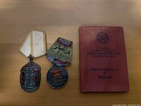Photo showing two USSR medals and a red certificate booklet on wood surface.