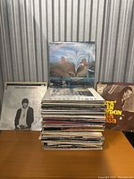 Stack of mixed vinyl record albums with various covers showing some recognizable artists and titles.