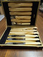 Open vintage box showing ten cocktail servers with stainless chromium plated serving parts and cream-colored nickel silver on plastic handles, wrapped partially in tissue paper