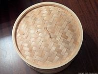 Bamboo dumpling stovetop cooker showing woven lid and three layers stacked.