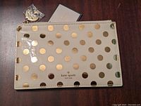 Front view of Kate Spade pencil pouch showing gold dots on cream background and logo in center bottom.