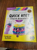 Front of the box of the kit showing title, knitting tool, sample charm bracelets made, and branding