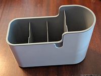 Gray kitchen utensil holder with rounded and rectangular compartments divided by vertical partitions seen from one angle.
