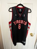Front view of black Toronto Raptors jersey with #6 and Adidas logo showing condition and design.