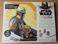 Front of box showing Mandalorian holding Grogu with kit details and paintbrush image.