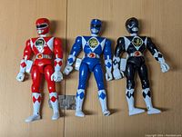 Three 1993 Bandai Power Rangers action figures in red, blue, and black, displayed standing against a wall, showing front view with clear details of each figure's costume and helmet.