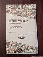 Front packaging of the Bread Story Reusable Bee's Wrap, displaying bakery-themed designs and product details including size 12x12 inches, 2 wraps with buttons, eco-friendly and washable.