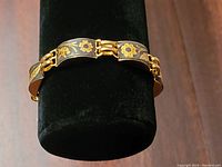 Front view of the gold-tone bracelet wrapped around a display stand showing detailed floral patterns on black enamel background.
