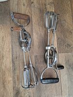 Two vintage hand mixers with metal beaters and wooden handles placed on wooden surface.