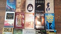 Photo showing 13 paperback books laid out on a table including titles by Arthur C. Clarke, Nicholas Sparks, John Nichols, and others.
