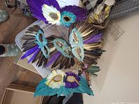 Six colorful feather masks with gold metallic trim laid out on a white surface.