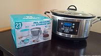 Photo shows the boxed 23-piece Farberware mix, measure and storage set and a Hamilton Beach programmable crockpot next to it on a black surface.