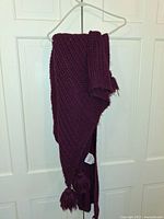 Full view of burgundy knitted lap throw folded and hanging on a clothes hanger against a white panel door.