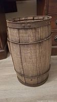 Full view of tall cylindrical vintage wooden barrel with metal bands and rivets, used for storing nails.