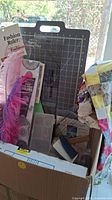Overall view of box containing sewing tools, quilt top, threads, rulers and accessories in a cardboard box.